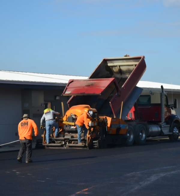 what is asphalt: Construction worker operating a yellow Dynapac roller to compact fresh asphalt on a residential paving project