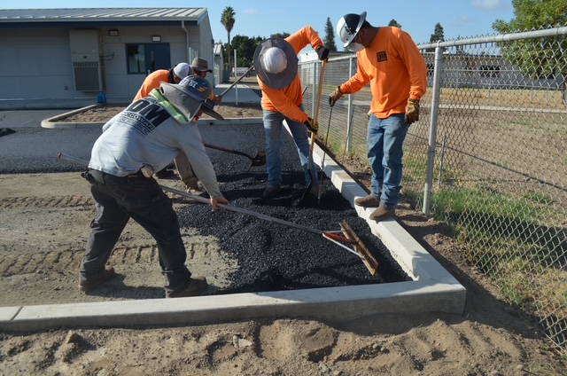 Crew of four asphalt contractor in visalia manually raking and leveling hot mix asphalt during a commercial installation