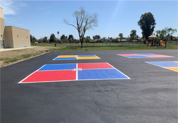 Brightly painted asphalt playground court featuring red, blue, and yellow squares for school recreational games