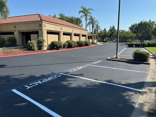 Freshly sealed asphalt parking lot featuring white compact car stencils and red fire lane curb compliance painting