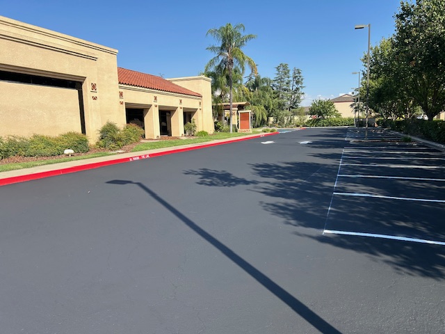 Newly paved commercial parking lot lane with white directional traffic arrows and red safety curb markings