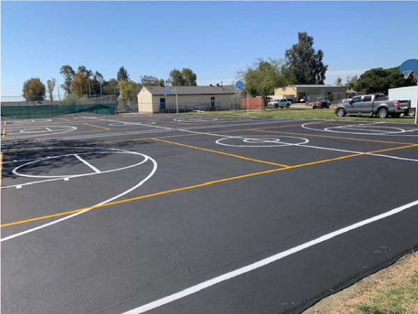 Outdoor recreational area featuring multiple basketball courts with crisp white and yellow game line striping on black asphalt