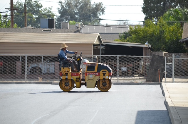 Professional operator driving a heavy vibratory roller to ensure proper density on a new asphalt paving job