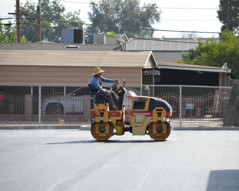 asphalt contractor in porterville, ca smoothing and compacting a freshly laid, dark asphalt surface using a heavy-duty Dynapac double-drum roller.