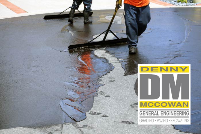 Professional asphalt maintenance crew applying protective liquid sealcoating onto a paved driveway surface using large squeegees, featuring the Denny McCowan General Engineering logo.