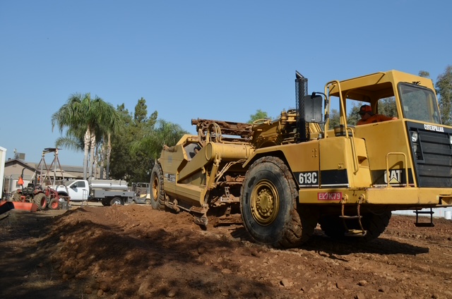 CAT scraper moving and grading soil during site preparation near a residential property in the central valley